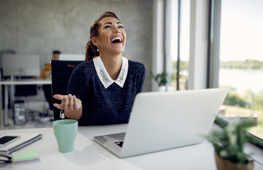 Woman laughing at her laptop in a bright office, discussing B2B SaaS strategies with her fractional CMO